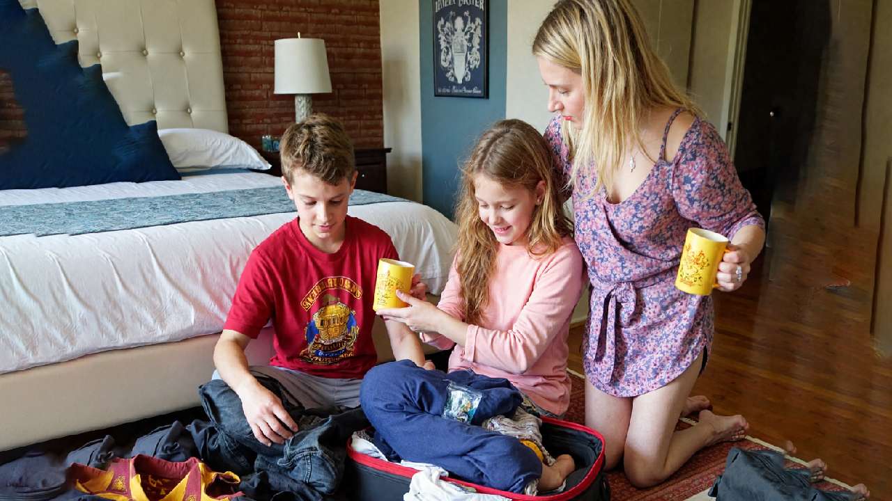 A family packing their bags for a Harry Potter trip, with wizarding items like wands, robes, and Butterbeer mugs scattered around. The cozy room has a magical travel vibe, capturing the excitement and anticipation of their upcoming adventure in the wizarding world. 