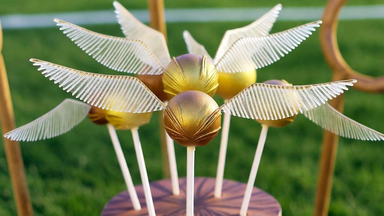 Golden Snitch Cake Pops with gold chocolate and candy wings, displayed on a Quidditch-themed stand for a Harry Potter party.