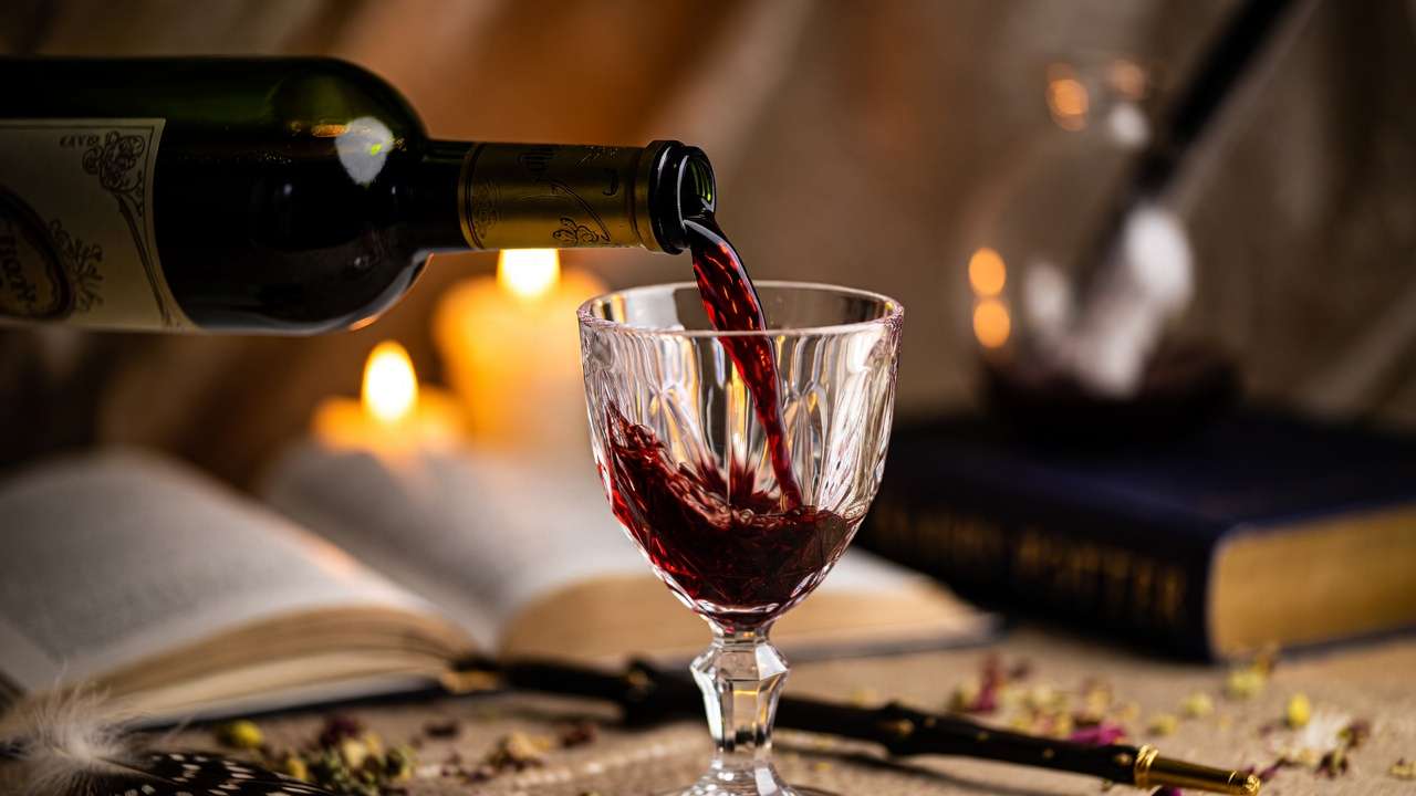 Magical pouring of Harry Potter themed red wine into a crystal goblet with candlelight and wizarding elements