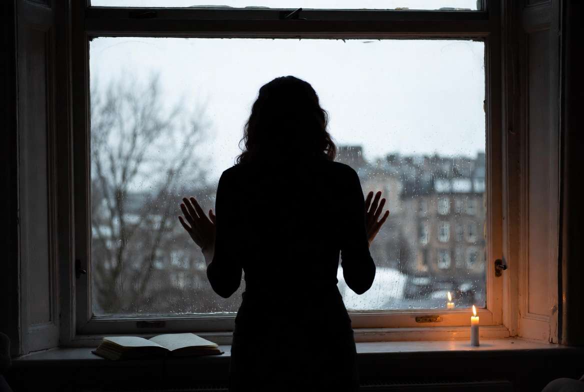 Silhouette of a woman at a rainy window reflecting the grief and hardship J.K. Rowling faced while writing Harry Potter