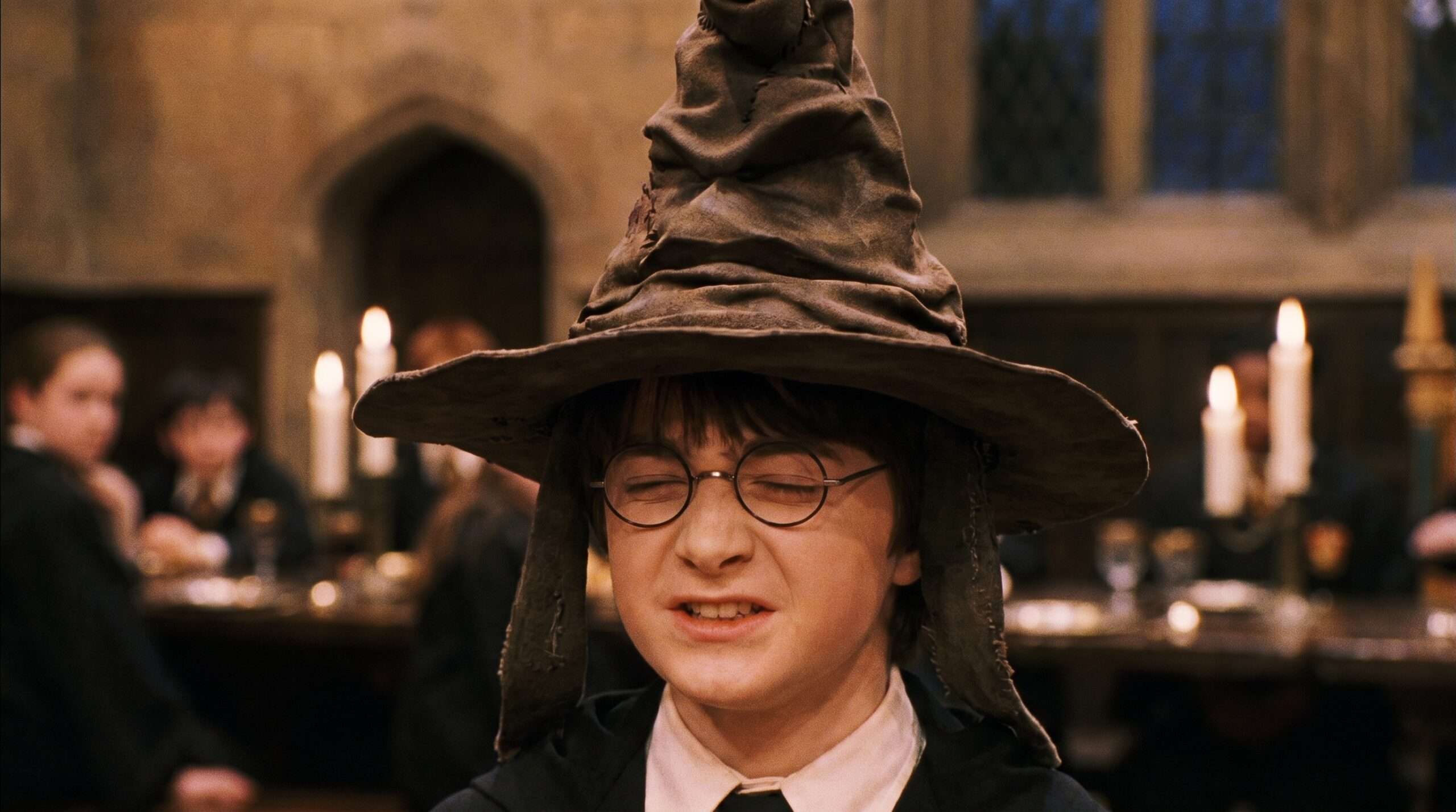 Close-up of a young Harry Potter wearing the Sorting Hat making a silent choice over his Hogwarts house during the sorting ceremony.