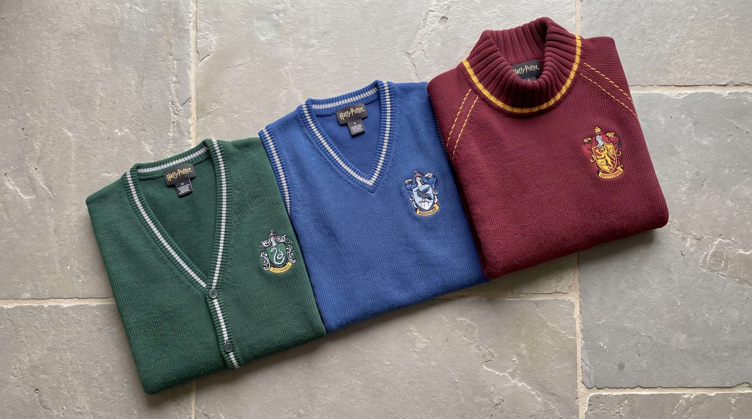 An editorial flat-lay showcasing Lochaven's diverse licensed Harry Potter knitwear range: Slytherin cardigan, Ravenclaw slipover, and Gryffindor Quidditch jersey.